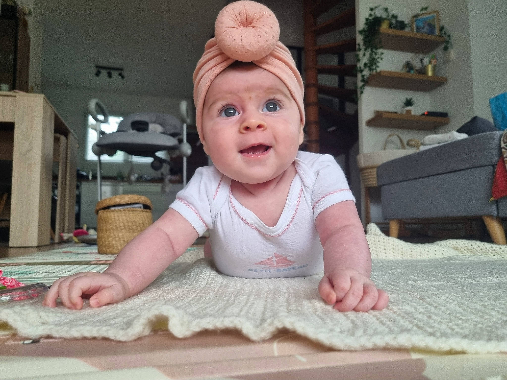 Elise participe au concours pour gagner de l'argent avec cette photo : baby, baby_toddler_clothing, carpet, cheek, child, crawling, floor, flooring, happy, hardwood, headwear, houseplant, linens, organ, person, pink, room, sitting, skin, smile