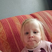 Lina participe au concours pour gagner de l'argent avec cette photo : toddler, child, blonde, face, expression, couch, striped_couch, indoors, portrait, sitting, clothing, heart_pattern, pink_shirt, wall, home, furniture, cute, young_child, person