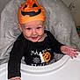 baby, child, halloween, pumpkin_hat, high_chair, smile, orange, black_clothing, cute, indoor, infant, face, hand, table, costume, holiday, celebration, portrait, person, seat