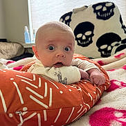 Myles joined the competition — help win amazing prizes! baby, bedroom, blanket, clothing, cozy, cushion, expression, face, hand, indoor, infant, light, orange, person, pillow, resting, skull_pattern, soft_texture, wide_eyes, window