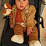 baby, child, stroller, plush_toy, brown_clothing, jacket, socks, indoors, floor_tiles, curious_expression, face, person, footwear, seated, toy, hand, mocha_hair, soft_toy, baby_clothes, black_stroller