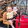 Lise a rejoint le concours — aidez-le/la à gagner de superbes lots ! toddler, child, glasses, carousel, ride, red_car, seatbelt, yellow_shirt, pink_shorts, shoes, playground, fun, smile, amusement_park, seat, steering_wheel, background_children, ornate, lights, daylight