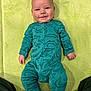 baby, infant, smiling, onesie, dinosaur_pattern, green_blanket, lying_down, child, cute, happy, face, person, clothing, soft_texture, indoors, portrait, young_child, cozy, baby_clothes, small_hands
