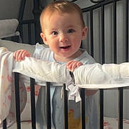 Ariella joined the competition — help win amazing prizes! baby, crib, infant, child, nursery, padded_rail, bedding, hand, smile, curious, standing, indoors, soft_light, cute, person, face, head, clothing, room, furniture