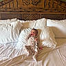 baby, bed, carved_wood, child, comfort, cozy, cute, floral_onesie, furniture, happy, indoor, infant, pillow, portrait, resting, sleepwear, smiling, white_bedding, wooden_headboard, young_child