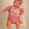adorable, baby, bow, child, cute, expression, face, feet, hands, headwear, indoors, infant, knitwear, pink_clothing, portrait, ropes, sitting, studio, swing, wooden_swing