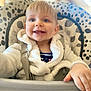 toddler, baby, high_chair, smiling, child, white_jacket, blue_eyes, indoor, seatbelt, cute, happy, face, hand, pattern, soft_lighting, portrait, infant, clothing, baby_furniture, closeup
