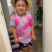 Génesis joined the competition — help win amazing prizes! child, smiling, straw_hat, tiedye_shirt, shorts, indoor, happy, person, floor, plant, toy, door, rug, sandals, jewelry, necklace, earrings, wooden_floor, home, casual_clothing