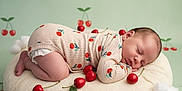 Mira participe au concours pour gagner de l'argent avec cette photo : baby, sleeping, onesie, cherry_pattern, cushion, fluffy, red_cherries, cotton_clouds, background, infant, peaceful, cute, soft_texture, child, newborn, pose, decor, studio, photography, resting