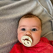 Lila a rejoint le concours — aidez-le/la à gagner de superbes lots ! baby, pacifier, blanket, red_clothing, face, infant, cute, portrait, eyes, soft_texture, child, indoors, cozy, expression, newborn, head, lying_down, skin, young_child, closeup