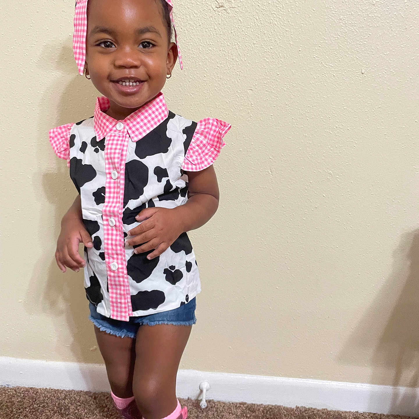 K Yana is registered to the contest to win money with this photo: carpet, child, clothing, cow_print, cute, denim_shorts, earrings, fashion, girl, happy, headband, indoor, pink_boots, pink_bow, portrait, shirt, smiling, standing, toddler, wall