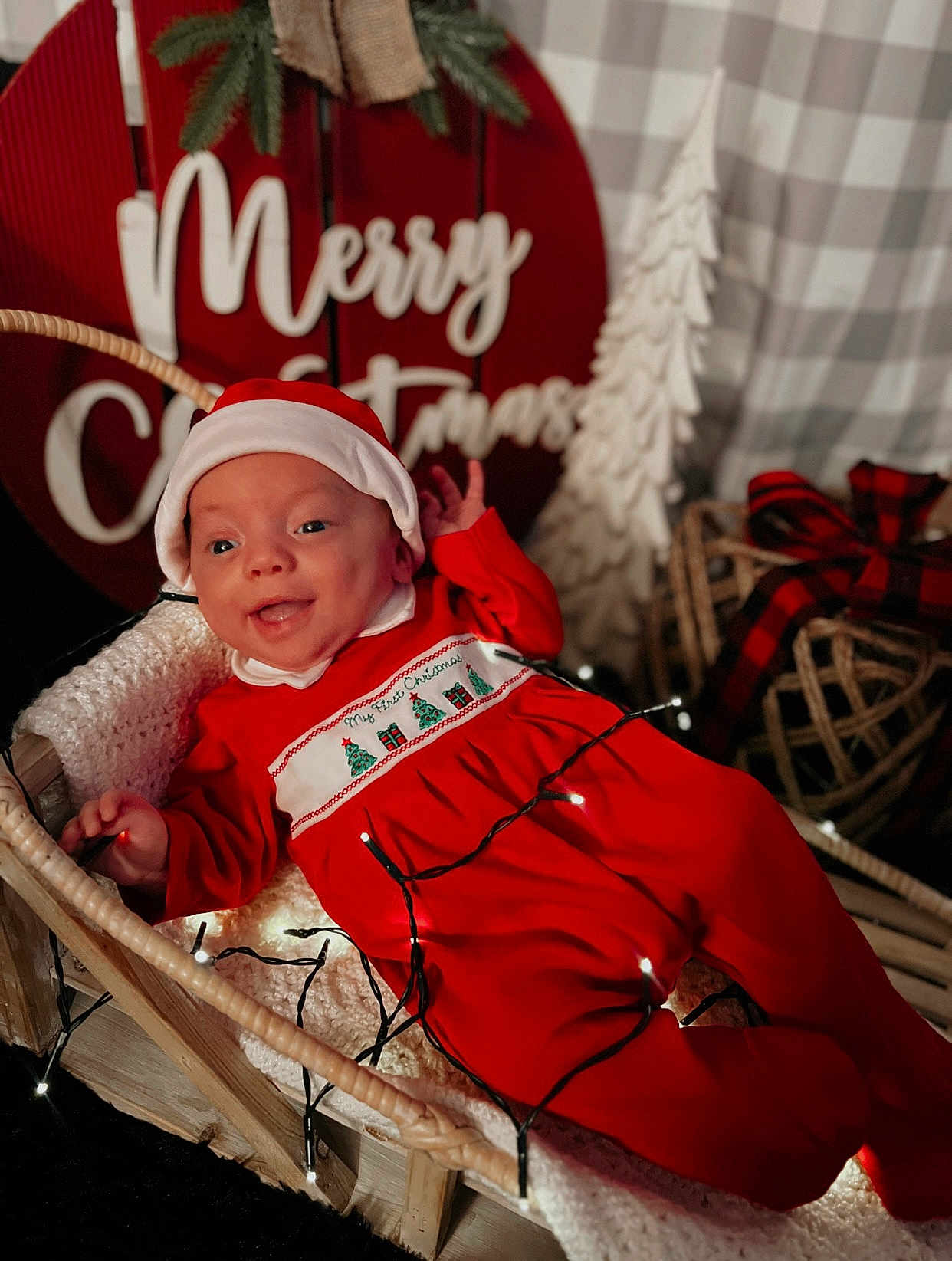 Kohen is registered to the contest to win money with this photo: baby, infant, christmas, holiday, festive, red_clothing, santa_hat, basket, blanket, fairy_lights, decorations, merry_christmas_sign, smiling, indoors, cozy, cute, portrait, celebration, seasonal, happy