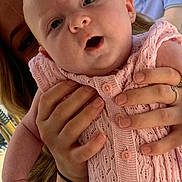 Tallulah is registered to the contest to win money with this photo: baby, infant, person, adult, hands, pink_clothing, knitwear, outdoor, daylight, casual, glasses, seated, curious, closeup, portrait, skin, face, expression, holding, background