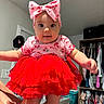 baby, child, infant, portrait, red_dress, ruffled_dress, pink_bow, headband, cherry_pattern, smiling, indoor, closet, clothing, wardrobe, laundry_basket, dresser, home, sitting, arms_outstretched, fashion