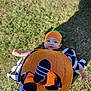 baby, pumpkin, costume, orange, grass, blanket, outdoor, cute, child, footwear, headwear, playful, fall, autumn, holiday, festive, smiling, person, lying_down, seasonal