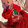 Kiely is registered to the contest to win money with this photo: baby, infant, pacifier, red_clothing, christmas, holiday, blanket, soft, cute, newborn, face, hand, tulle_skirt, patterned_fabric, lying_down, indoors, closeup, person, festive, celebration