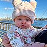 baby, child, hat, knit_hat, bear_ears, floral_clothing, outdoor, waterfront, sky, clouds, person, holding, hand, portrait, cute, infant, warm_clothing, daylight, blue_sky, nature