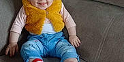 Inaya participe au concours pour gagner de l'argent avec cette photo : baby, child, clothing, couch, cute, face, furniture, happy, home, indoor, infant, jeans, person, radiator, seated, shoes, smiling, socks, vest, wooden_wall