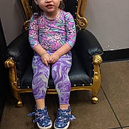 Elizabeth is registered to the contest to win money with this photo: toddler, child, girl, hair_buns, purple_leggings, floral_top, blue_shoes, chair, black_and_gold, floor_tiles, indoor, smile, playful, fashion, portrait, seated, young_child, casual_clothing, cute, happy