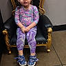 toddler, child, girl, hair_buns, purple_leggings, floral_top, blue_shoes, chair, black_and_gold, floor_tiles, indoor, smile, playful, fashion, portrait, seated, young_child, casual_clothing, cute, happy