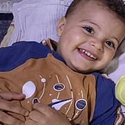 Moumouh participe au concours pour gagner de l'argent avec cette photo : toddler, smiling, child, curly_hair, face, dimples, blue_clothing, brown_clothing, space_design, hand, fingers, lying_down, blanket, happy, portrait, indoors, cute, young_child, bright_eyes, cozy