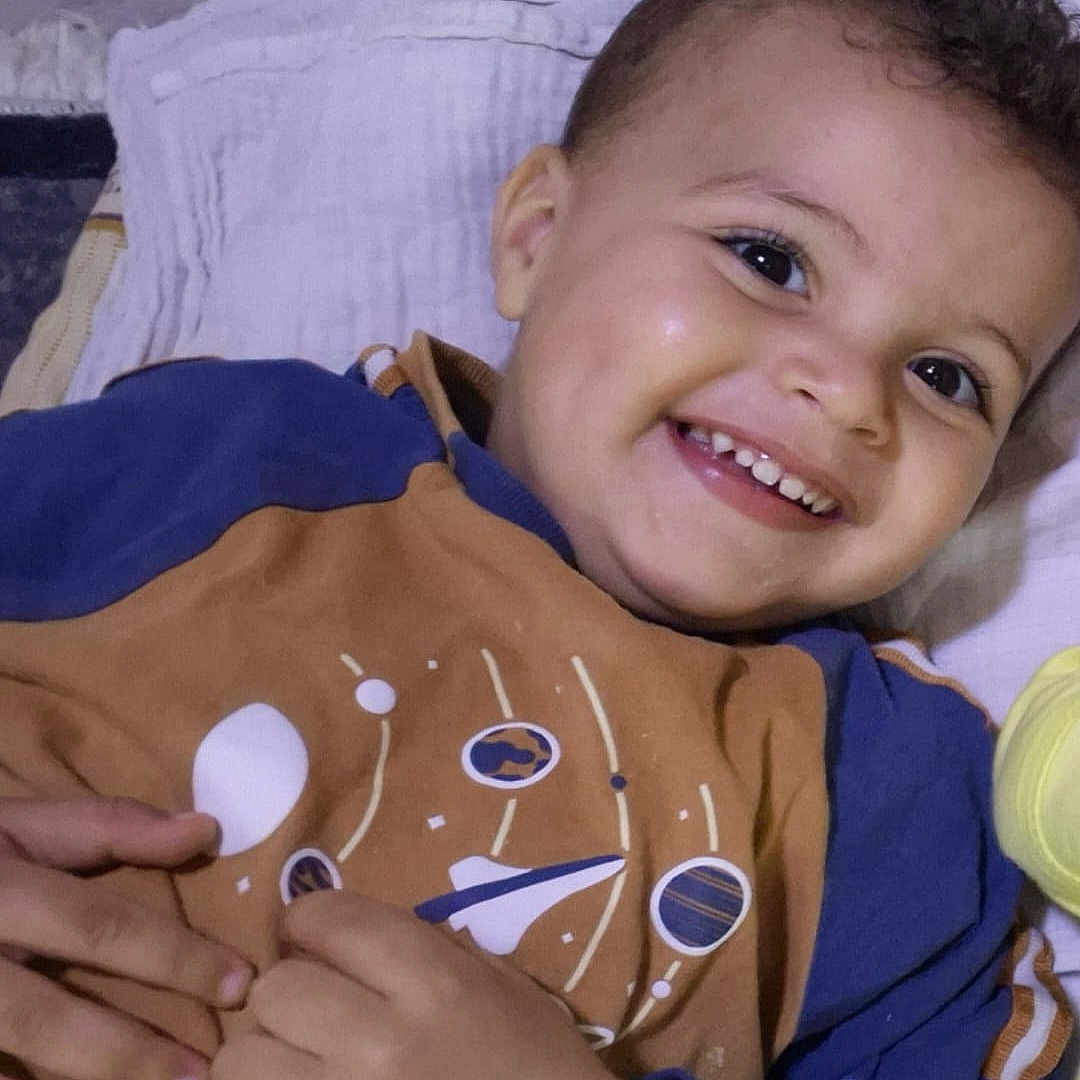 Moumouh participe au concours pour gagner de l'argent avec cette photo : blanket, blue_clothing, bright_eyes, brown_clothing, child, cozy, curly_hair, cute, dimples, face, fingers, hand, happy, indoors, lying_down, portrait, smiling, space_design, toddler, young_child