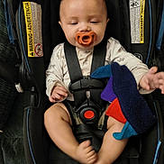 Esidro is registered to the contest to win money with this photo: baby, pacifier, car_seat, child, toy, plush_toy, straps, infant, seat_belt, hand, foot, clothing, warning_label, fabric, comfort, indoor, cute, small_child, safety, snugride