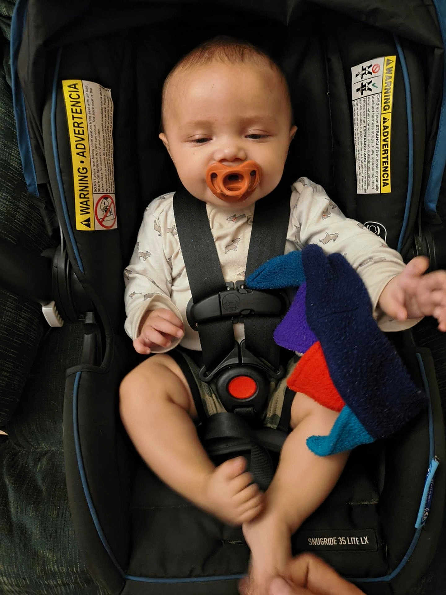 Esidro is registered to the contest to win money with this photo: baby, pacifier, car_seat, child, toy, plush_toy, straps, infant, seat_belt, hand, foot, clothing, warning_label, fabric, comfort, indoor, cute, small_child, safety, snugride