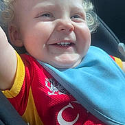 Cohen is registered to the contest to win money with this photo: toddler, child, smiling, curly_hair, blue_eyes, car_seat, bib, red_shirt, yellow_shirt, happy, portrait, indoor, closeup, baby, clothing, seatbelt, cute, person, infant, sunlight