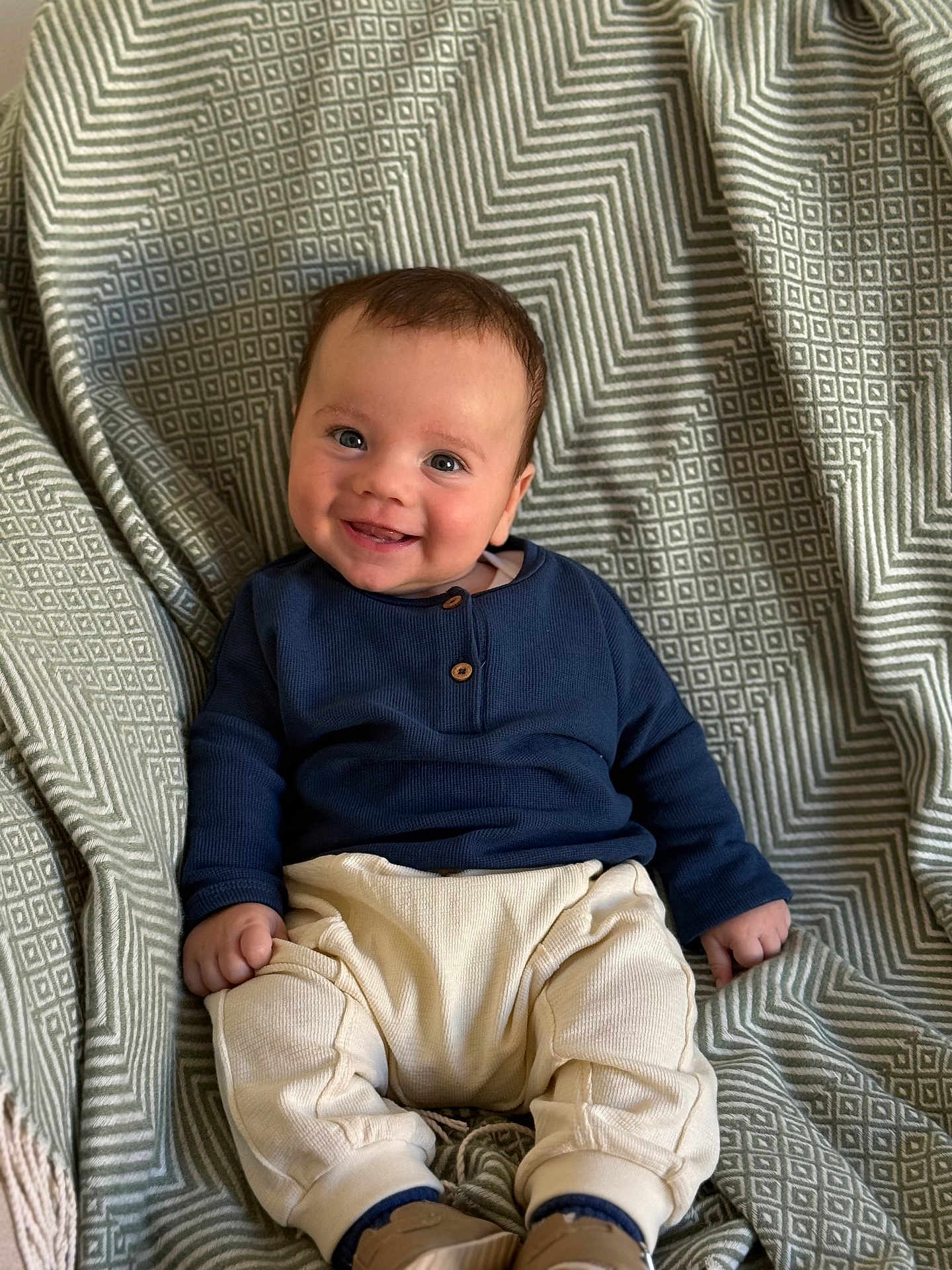 Oakley joined the competition — help win amazing prizes! baby, smiling, child, infant, sitting, blue_shirt, cream_pants, blanket, patterned_blanket, happy, cute, indoors, portrait, young_child, small_hands, footwear, cozy, comfortable, face, person