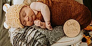 Mckenna joined the competition — help win amazing prizes! newborn, baby, sleeping, knitted_hat, brown_wrap, white_chair, gray_blanket, pillow, cartoon_animals, wooden_plaque, one_month, marquee_light, vintage, cozy, indoor, portrait, cute, milestone, resting, decor