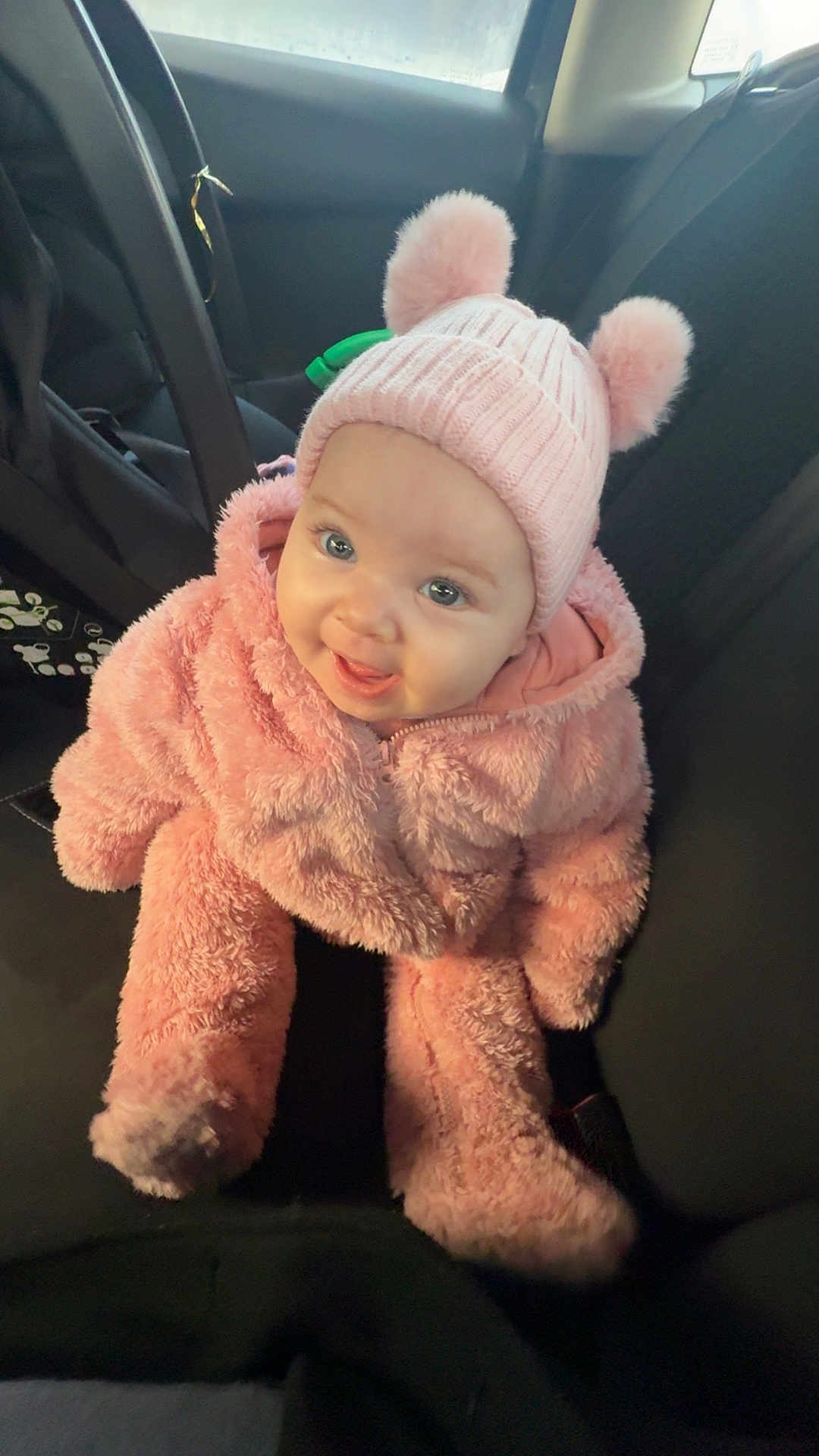Leya a rejoint le concours — aidez-le/la à gagner de superbes lots ! baby, child, pink_clothing, hat, pom_poms, car_seat, smiling, happy, cute, indoor, seat, clothing, person, portrait, warm, fuzzy, infant, headwear, cozy, car_interior