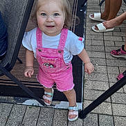 Violet joined the competition — help win amazing prizes! toddler, child, smiling, pink_overalls, bow, toy_story, outdoor, patio, footwear, sandals, sneakers, person, happy, standing, pavement, chair, legs, casual, daylight, expression