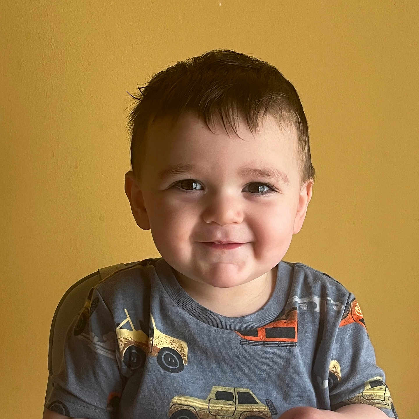 Joseph Anthony is registered to the contest to win money with this photo: child, toddler, smile, happy, face, boy, short_hair, indoor, yellow_wall, shirt, clothing, toy_trucks, sitting, high_chair, snack, hands, cute, portrait, casual, person