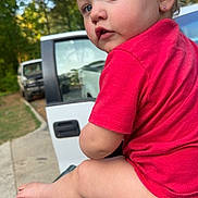 Sarah is registered to the contest to win money with this photo: toddler, child, red_shirt, diaper, outdoor, parked_cars, green_surface, curious, portrait, side_view, earrings, nature, trees, daylight, person, baby, short_hair, expression, sitting, side_profile