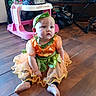 Sarah is registered to the contest to win money with this photo: baby, child, costume, pumpkin, orange, green, headband, floor, wooden_floor, toy_car, baby_walker, indoor, curious, sitting, footwear, dress, plaything, person, infant, cute
