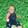 baby, cake, birthday, denim_overalls, frosting, messy, smiling, sitting, green_background, celebration, infant, food, face, hands, feet, party, colorful, sprinkles, cute, child
