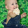 baby, child, cake, denim_overalls, frosting, smiling, messy, blue_eyes, sitting, green_background, leaf_pattern, happy, cute, one_year_old, face, hand, food, celebration, portrait, indoor
