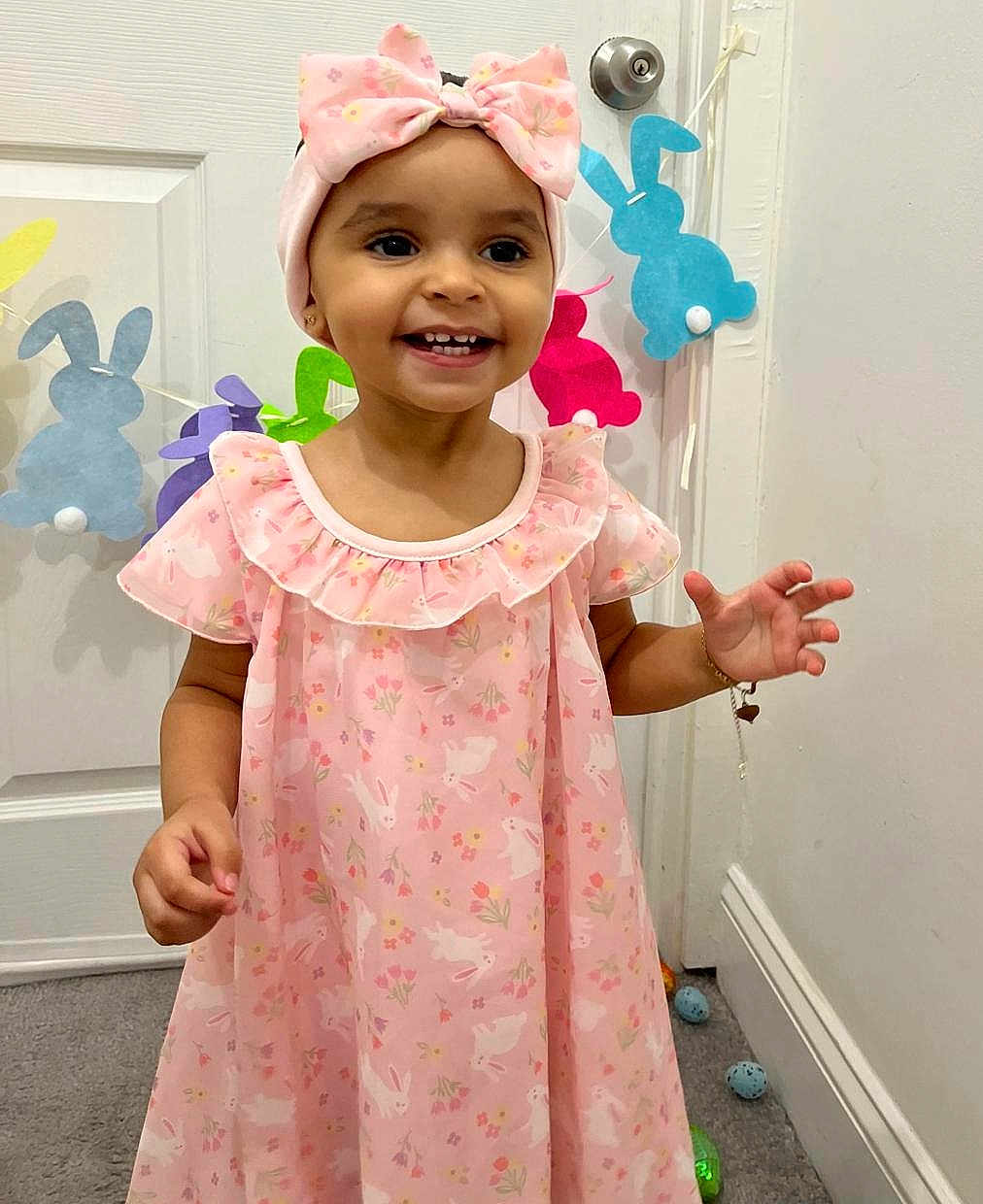 Merlyn joined the competition — help win amazing prizes! child, toddler, smiling, pink_dress, headband, bow, indoors, carpet, door, easter_eggs, bunny_decorations, happy, cute, portrait, person, accessory, jewelry, playful, celebration, holiday