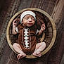 newborn, baby, sleeping, basket, wooden_floor, football_onesie, headband, infant, cute, peaceful, indoors, portrait, child, resting, small_feet, cozy, brown_clothing, wood_texture, baby_boy, adorable