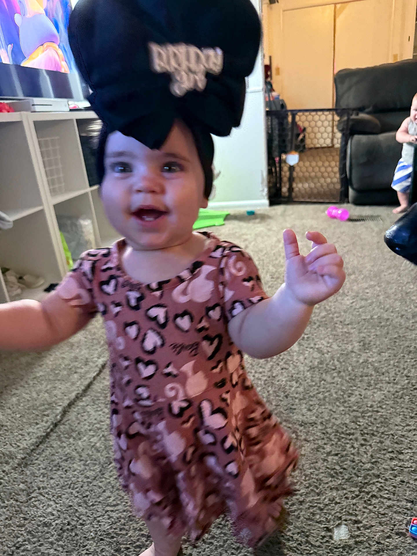 Kynlee joined the competition — help win amazing prizes! toddler, child, living_room, carpet, toy, baby_gate, sofa, black_bow, pink_dress, heart_pattern, smile, motion_blur, indoor, furniture, person, floor, baby, play, home, cute