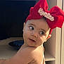 Kynlee is registered to the contest to win money with this photo: baby, child, headband, red_bow, face, curious, looking_away, sleeveless_clothing, indoor, furniture, shelf, person, portrait, cute, infant, skin, expression, young_child, clothing, headwear