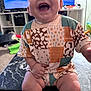 Zayden is registered to the contest to win money with this photo: baby, infant, child, smiling, laughing, patchwork_clothing, sitting, table, living_room, television, toy, carpet, furniture, indoor, happy, cute, chubby_legs, person, home, bright