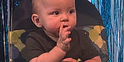 Zayden is registered to the contest to win money with this photo: baby, child, high_chair, pizza, party, table, green_tablecloth, plate, food, balloon, streamers, celebration, curious, indoor, cute, infant, face, hands, clothing, birthday