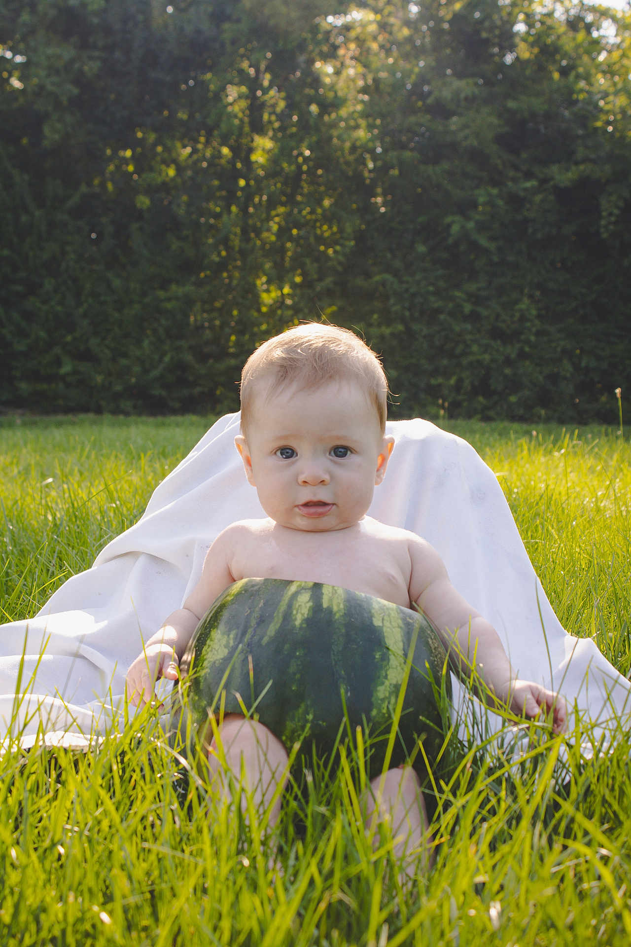 Bentley is registered to the contest to win money with this photo: baby, watermelon, grass, outdoor, nature, greenery, child, summer, sunlight, playful, cute, fruit, rind, shirtless, sitting, white_cloth, trees, park, portrait, daylight