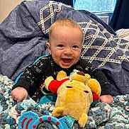 Bentley joined the competition — help win amazing prizes! baby, smiling, plush_toy, blanket, window, curtains, indoor, child, happy, knitted_blanket, toy, person, face, blue, red, yellow, furniture, light, cozy, cute