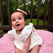 Mira is registered to the contest to win money with this photo: baby, infant, smiling, pink_bow, white_dress, blanket, outdoor, greenery, wooden_railing, happy, cute, portrait, child, sitting, feet, face, skin, nature, daylight, playful