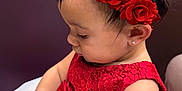 Liah is registered to the contest to win money with this photo: baby, infant, child, red_dress, floral_headband, earring, eyelashes, profile_view, sitting, hands, toy, pearl_belt, bow, closeup, portrait, indoor, blurred_background, cute, celebration, jewelry