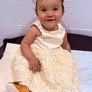 Liah joined the competition — help win amazing prizes! baby, infant, toddler, smile, headband, dress, white_dress, floral_skirt, pearl_trim, gold_shoe, hand, eyes, sitting, portrait, indoor, textured_wall, fabric, bench, cute, happy