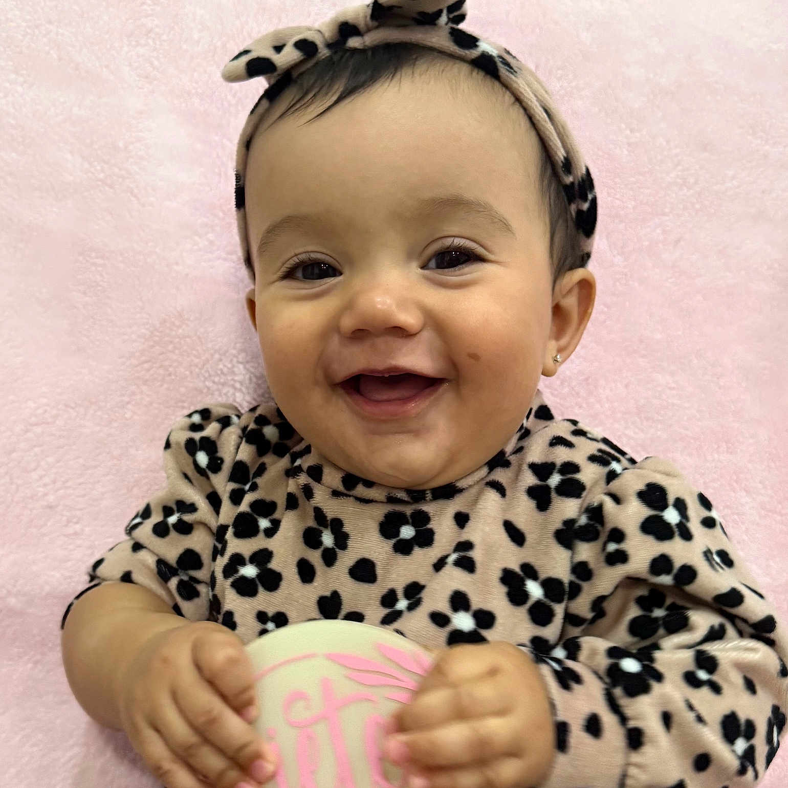 Liah joined the competition — help win amazing prizes! baby, blanket, bow, cheeks, close_up, earring, eyes, face, hands, happy, headband, holding_milestone, infant, leopard_print, mouth, outfit, pink_background, portrait, smiling, soft_texture